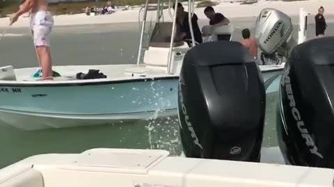 Girl revs boat engine sprays water on shirtless guy on other boat