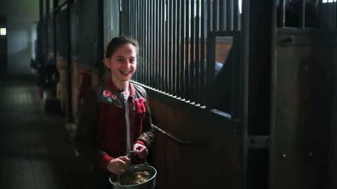 The girl feeds a horse in a stables look at camera smile funny