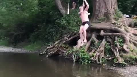 Shirtless man rope swing lands in shallow water