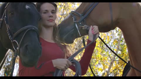 Caucasian girl with long brown hair holding bridles of two horses outdoors