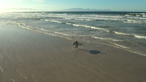 A Person Running at the Beach while Carrying a Surfboard