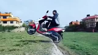 Man on red moped motorcycle drives over hill