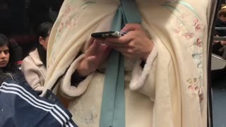 Woman wears white hood on subway train, "little white riding hood"