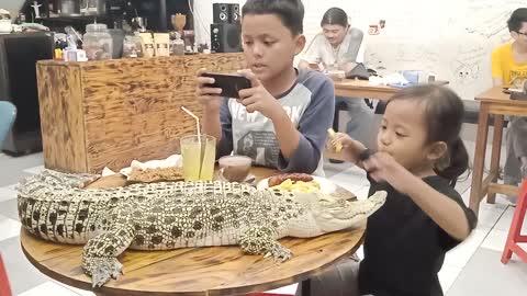 A little girl has dinner with her friend and a crocodile