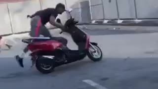 Guy does wheelie on moped bike in parking lot, scrapes floor and falls off