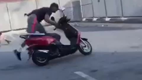 Guy does wheelie on moped bike in parking lot, scrapes floor and falls off