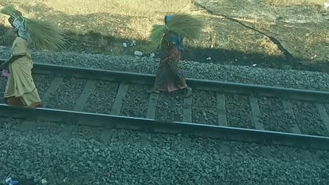 Two women with loads on their heads walk along the railway line.