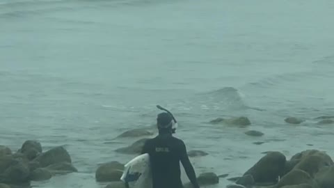 Man scuba gear with surf board walking on rocks