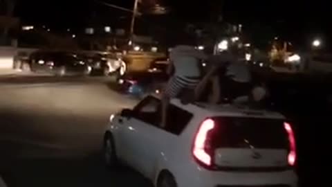Night time three guys on top of kia soul car paddling while car is moving driving