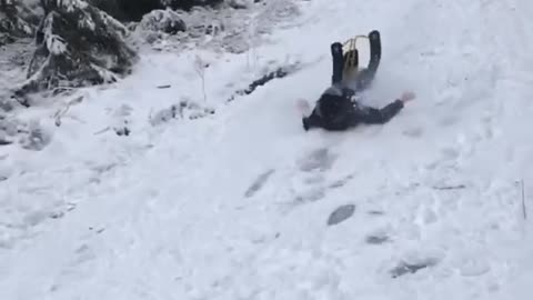 Guy goes sledding down slope on yellow sled and flies off