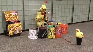 Person dressed up as alien yellow red antenna playing drums