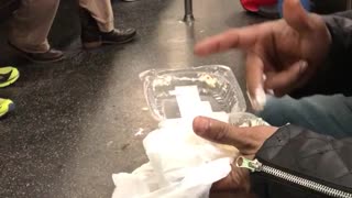 Guy in black jacket eating food with fingers on subway