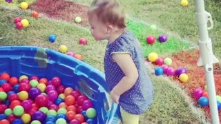 Little toddler dives into a pool full of rainbow colored balls!