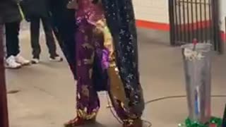 Man in sequin pants and sparkly red vest dances and sings in subway station