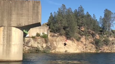 Two guys on bridge back flip into water