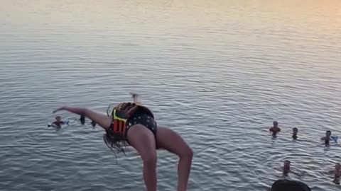 Girl in safety jacket does back flip off diving board into ocean
