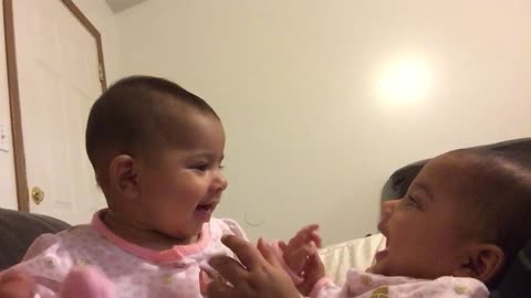 Baby twin girls laughing at each other