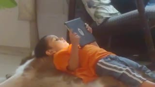 Little boy plays with tablet while lying on top of Golden Retriever