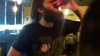 A guy drinks beer after balancing drink on a passed out guy in green