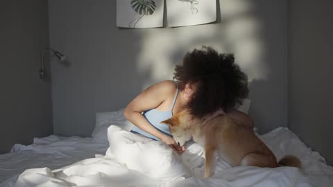A Woman Teasing Her Pet Dog With Food While In Bed