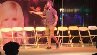 Music guy on stage in red plaid shirt and brown shorts face plants while dancing