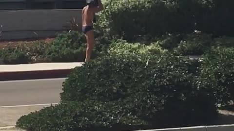 Guy in speedo carries surfboard on his head while barefoot