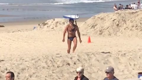 Guy in blue speedo balancing surfboard at beach