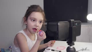 Little Girl Applying Lipstick While Looking At Her Smartphone