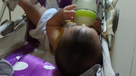 An 8-month-old baby holds a bottle of super cute milk