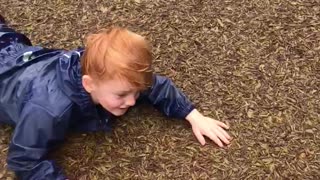 Little kid boy blue jump suit red hair goes down slide flies onto ground