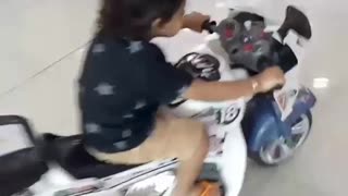 Little girl driving white toy motorcycle falls down