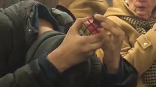 Guy does rubik's cube with head down without looking on subway train