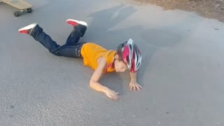Little boy in yellow shirt helmet falls off skateboard