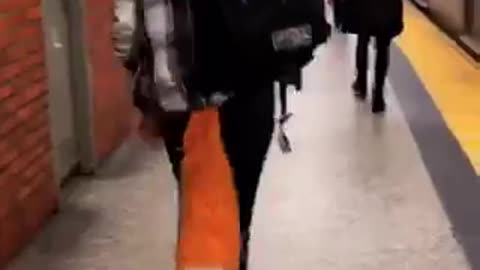 Woman walking in subway station wears big orange fox tail and ears