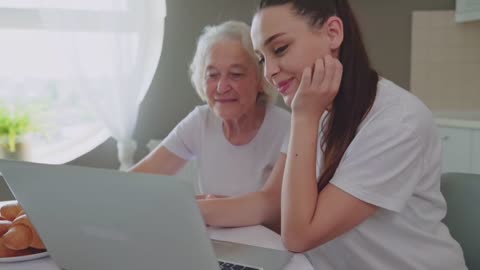 Young girl helps grandma to learn laptop
