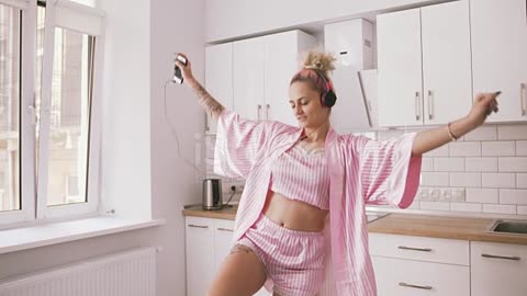 Happy young woman with pink hair dancing in kitchen wearing