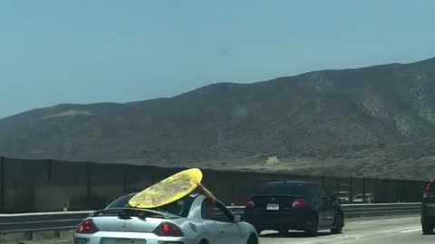 Yellow surf board on grey silver car roof