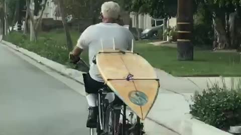Old man white hair driving bike with surfboard in back
