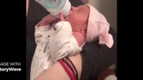 Adorable newborn baby preciously holds her own bottle