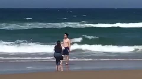 Woman taking pictures of shirtless man on beach