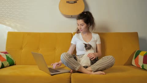 Young asian woman surfing in internet with her cat at home on coach