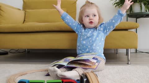 A Little Girl With A Book On Her Lap Flopping Her Hands up