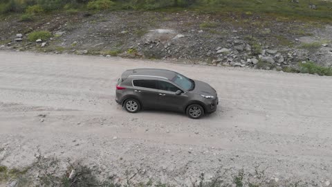 A drone flies behind a car in the tundra.