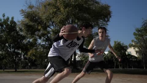 Two boys playing basketball at an outdoor court