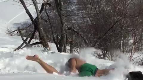 Shirtless guy snow boogie board jumps ramp and falls down
