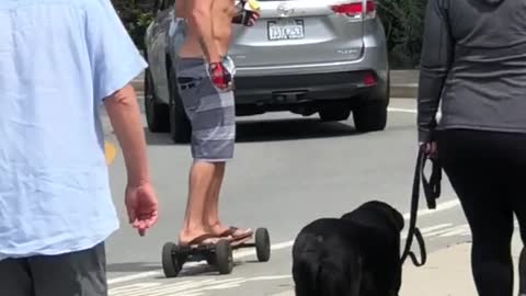Shirtless guy rides a motorized skateboard on side street
