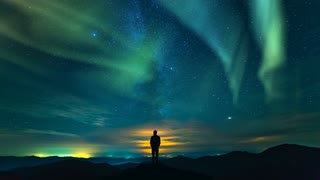 The man standing on the rock on the starry sky with a northern light background