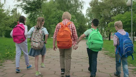 Children Walking On A Paved Pathway With Their Backpacks