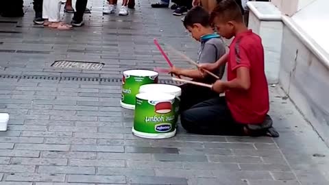 Two Boys Playing Drums Out Of Plastic Buckets