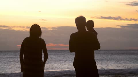 Silhouetted Family Walking Along Beach at Sunset